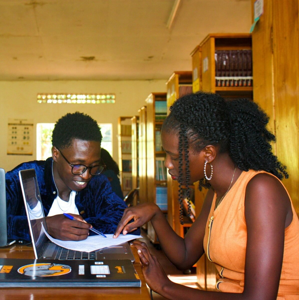 Casal analisando documentos financeiros juntos em uma biblioteca, com um notebook sobre a mesa.