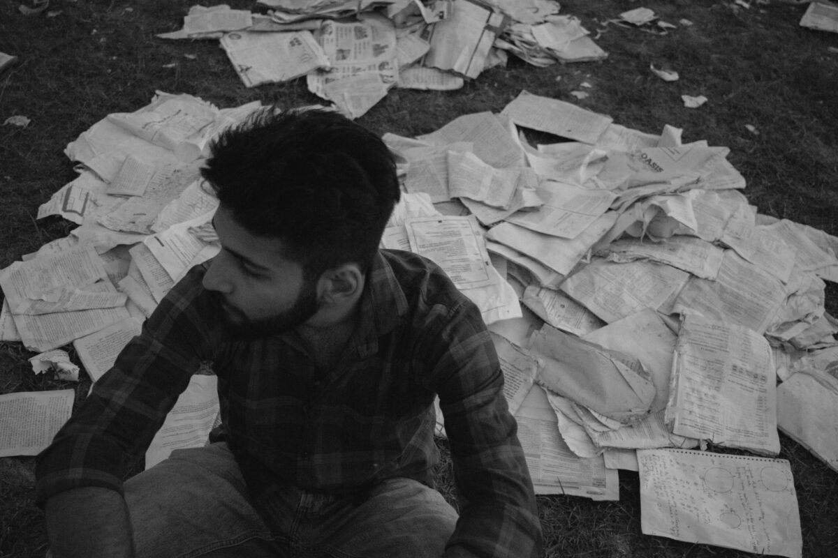 Homem cercado por contas e documentos, representando o ciclo de endividamento e dificuldades financeiras.