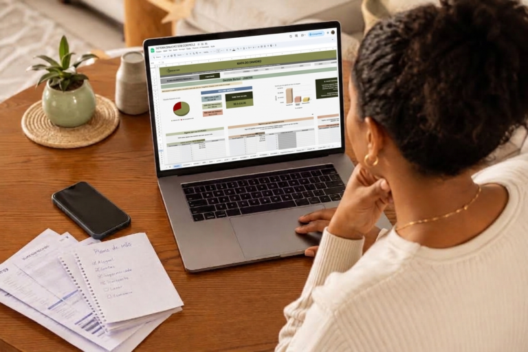 Mulher analisando planilha de controle financeiro no notebook, com anotações de contas ao lado